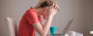 Stressed teenage student holding her head while studying at a laptop