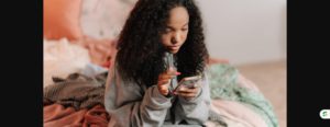 Teenage girl checking her smartphone while sitting on her bed